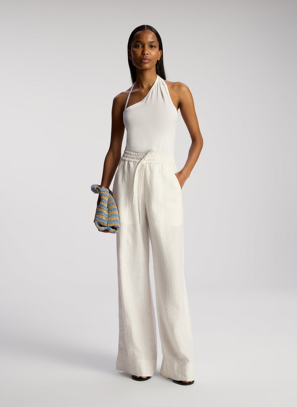 front view of woman wearing white asymmetric tank top and cream linen wide leg pants