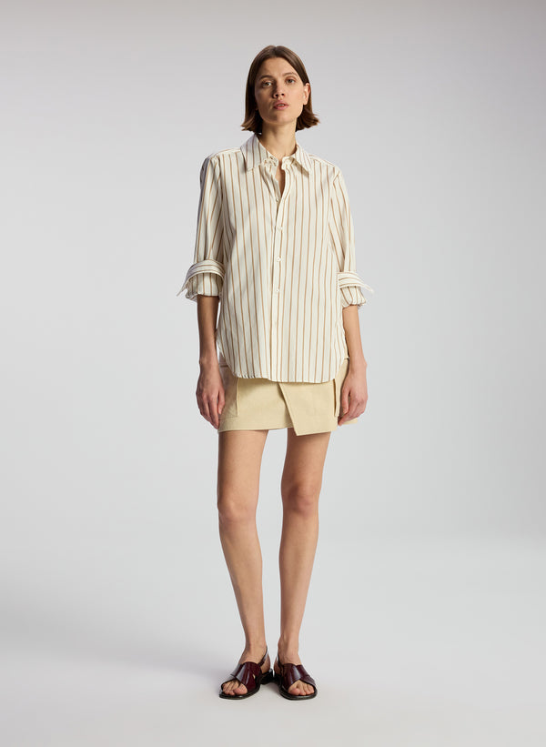 front view of woman wearing brown and white striped shirt and beige mini skirt