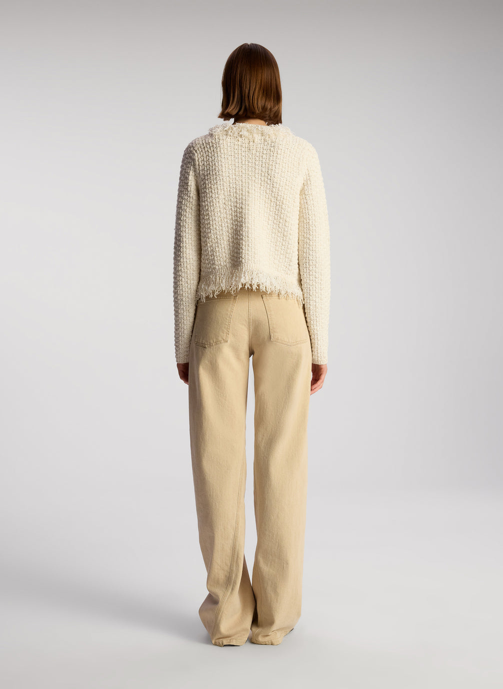 back view of woman wearing cream fringed cardigan and tan pants