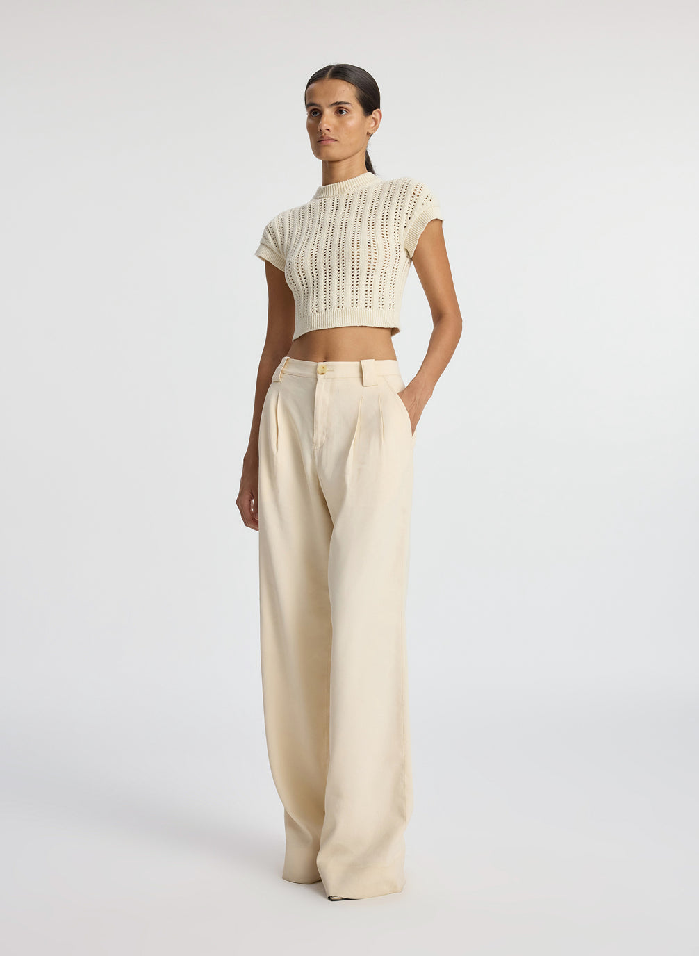 side view of woman wearing ivory short sleeve open weave top and beige wide leg pants