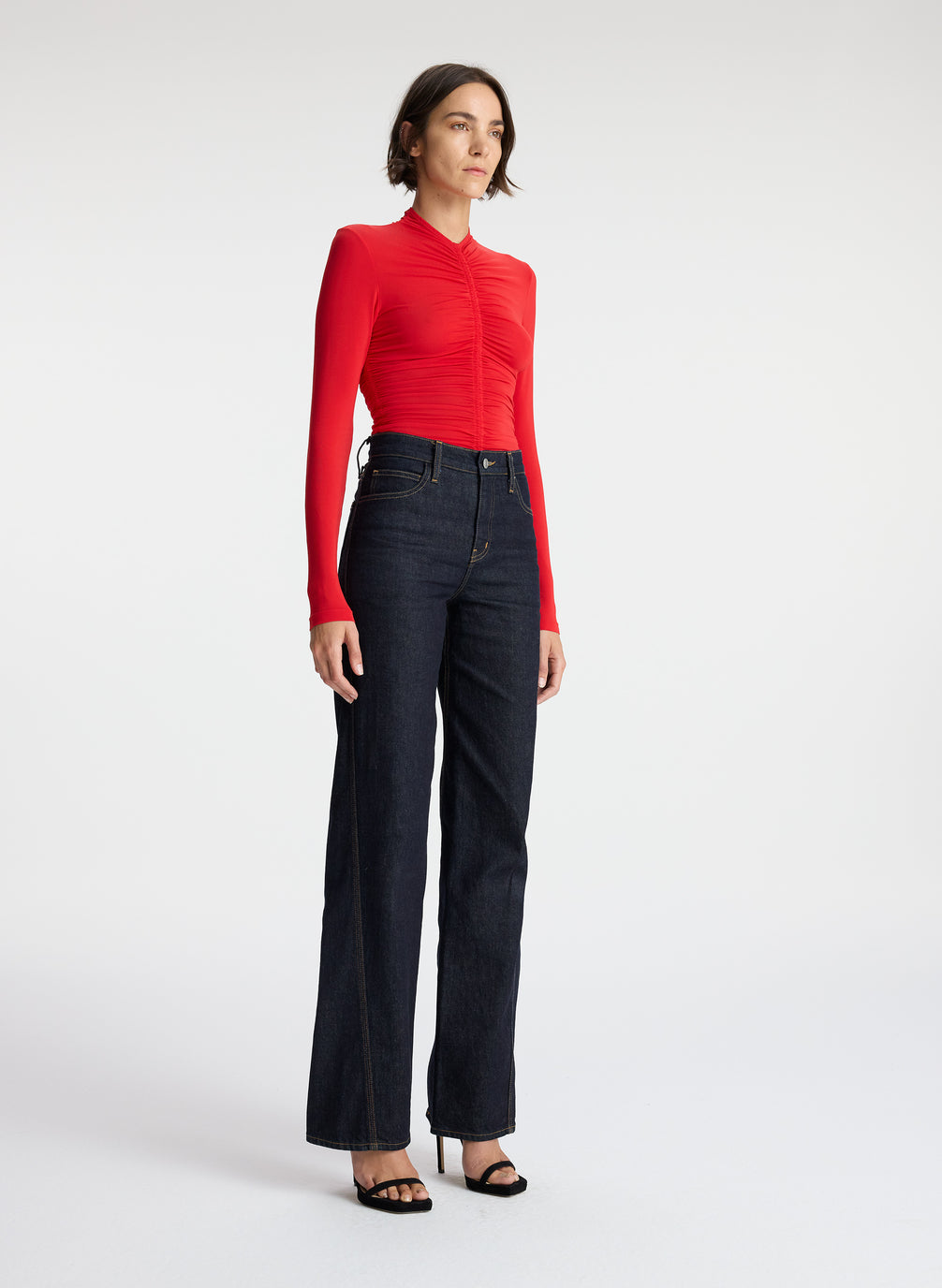 side view of woman wearing red ruched long sleeve top and dark wash jeans