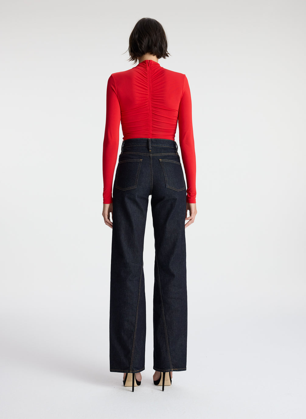 back view of woman wearing red ruched long sleeve top and dark wash jeans