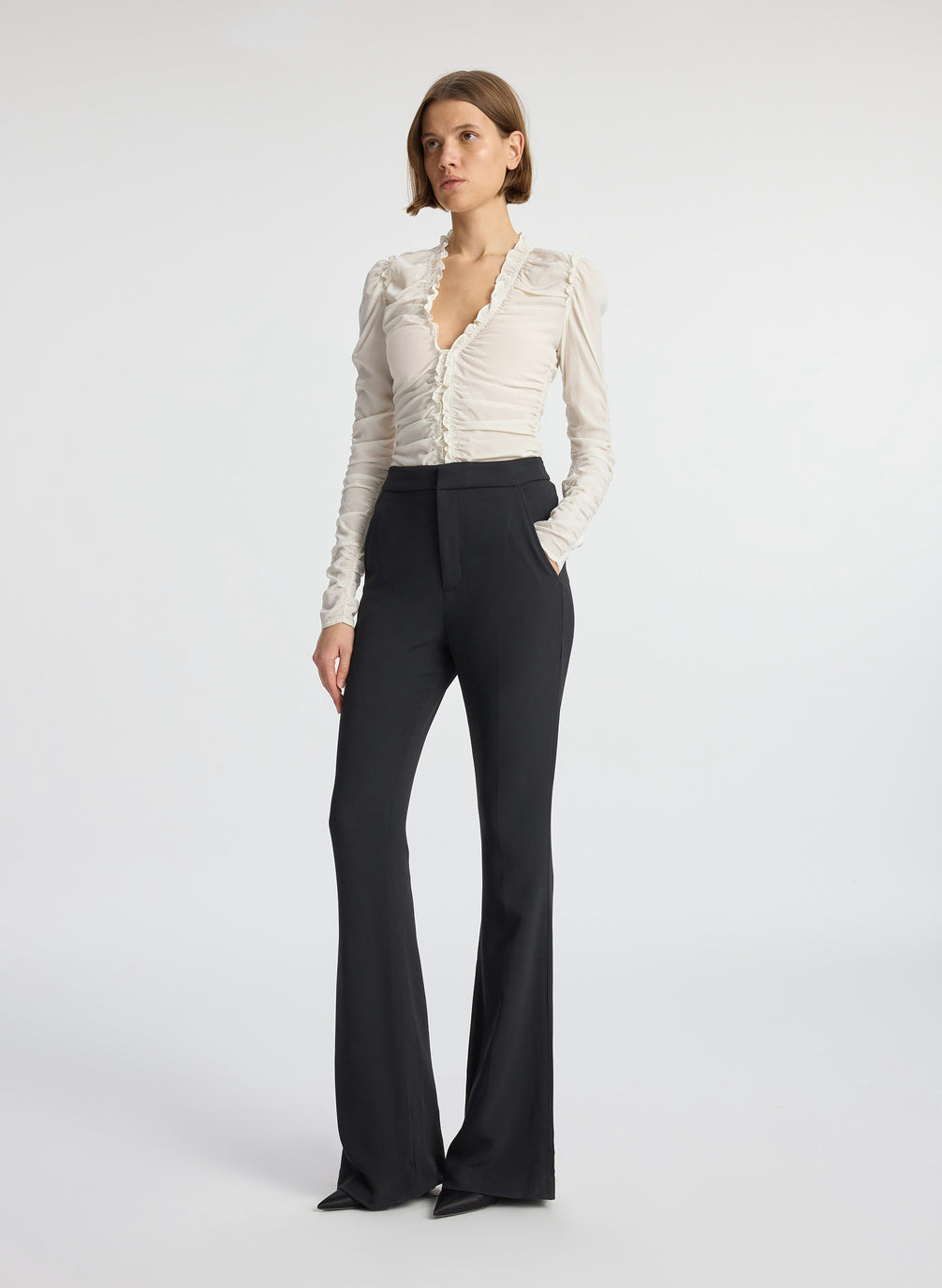 side view of woman wearing white long sleeve v neck top and black flared pants