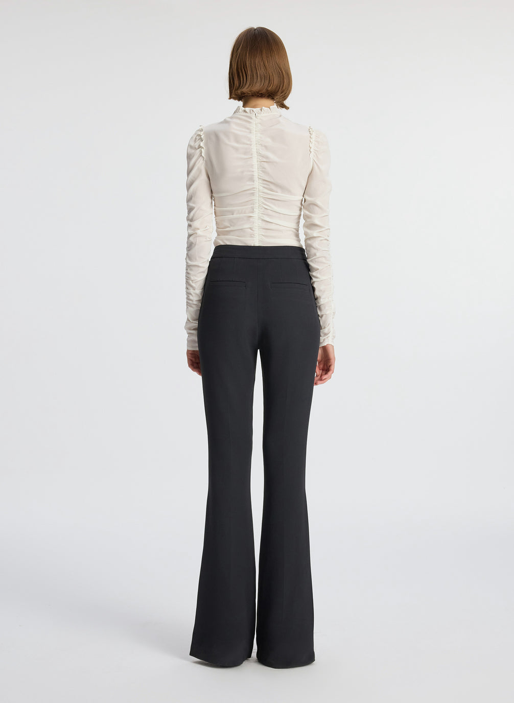 back view of woman wearing white long sleeve v neck top and black flared pants
