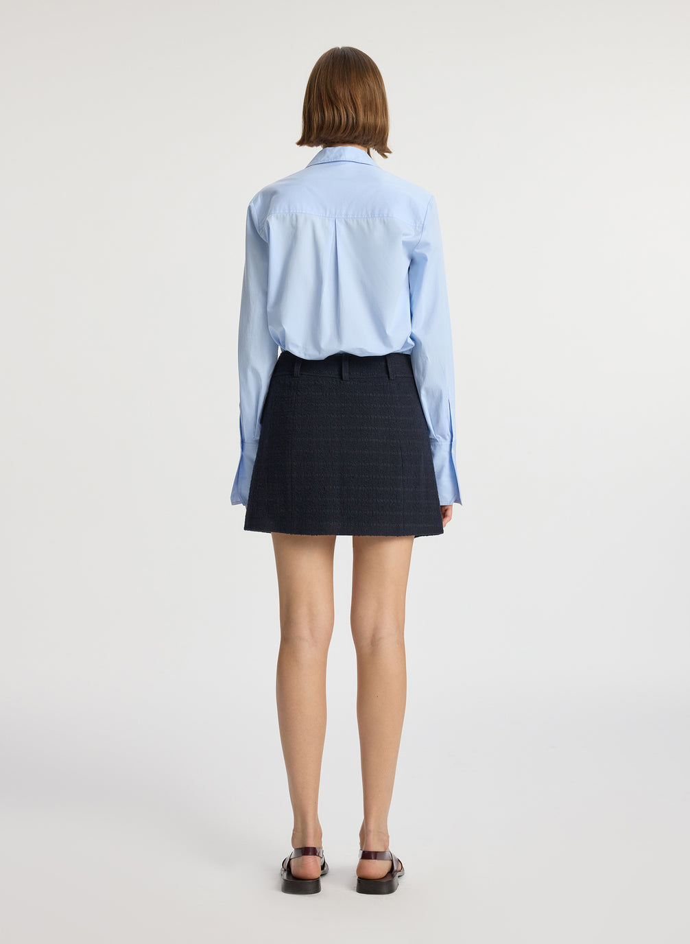 back view of woman wearing blue button down collared shirt and navy tweed mini wrap skirt 