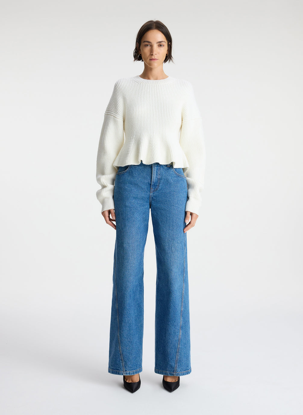 front view of woman wearing white peplum sweater and medium blue wash denim jeans