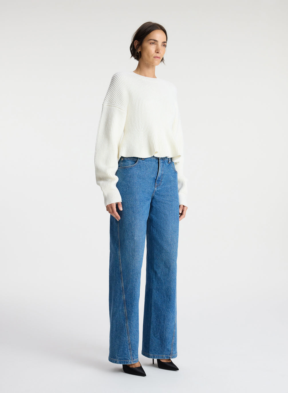 side view of woman wearing white peplum sweater and medium blue wash denim jeans