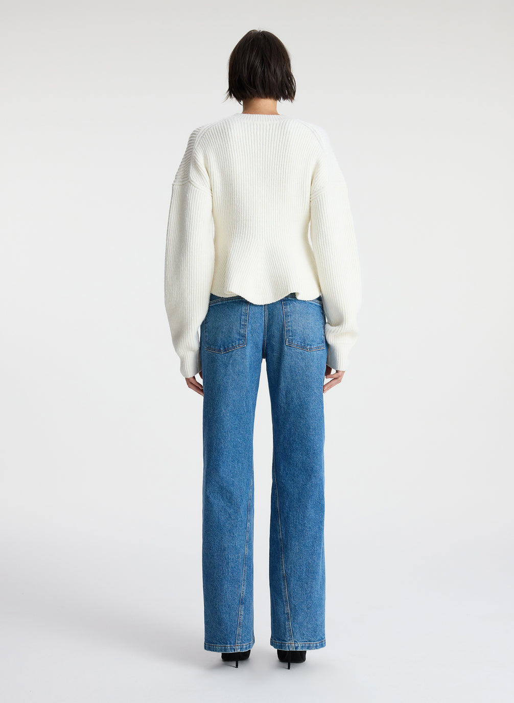 back view of woman wearing white peplum sweater and medium blue wash denim jeans