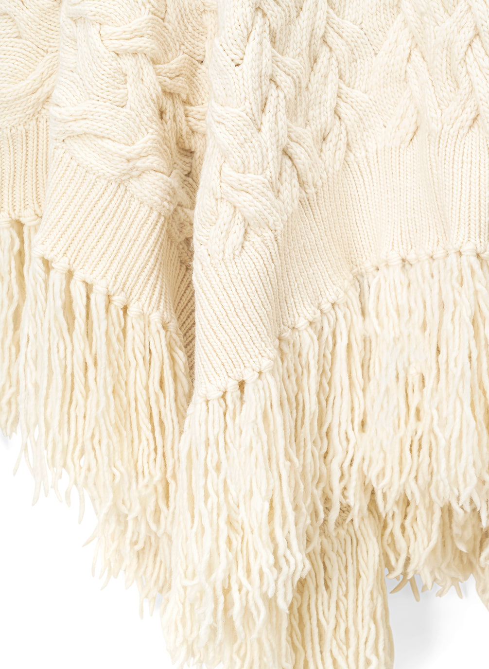 detail view of woman wearing cream cable knit poncho with fringe