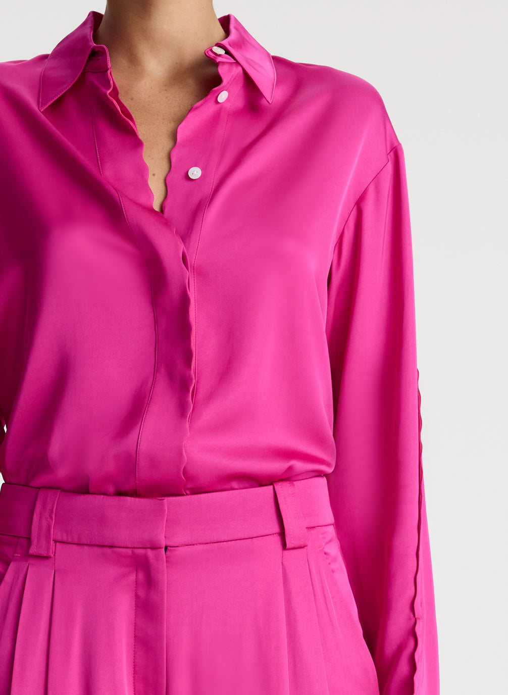 detail view of woman wearing bright pink scalloped detailed long sleeve satin shirt and bright pink pants