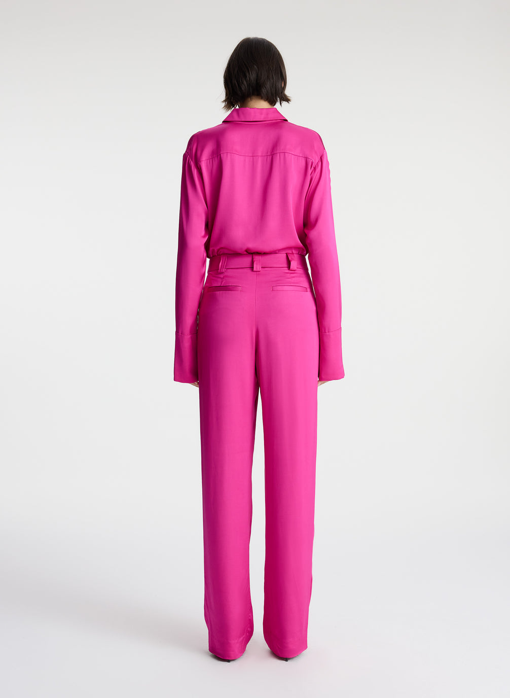 back view of woman wearing pink button down collared satin long sleeve shirt with matching pink satin pants