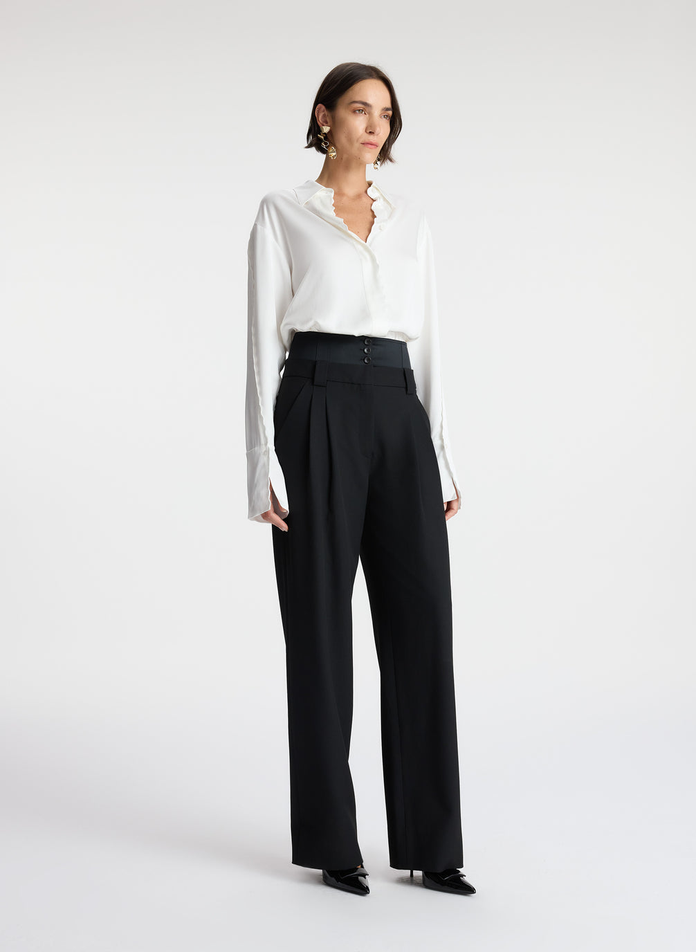 side view of woman wearing white scalloped detailed long sleeve top and black pants