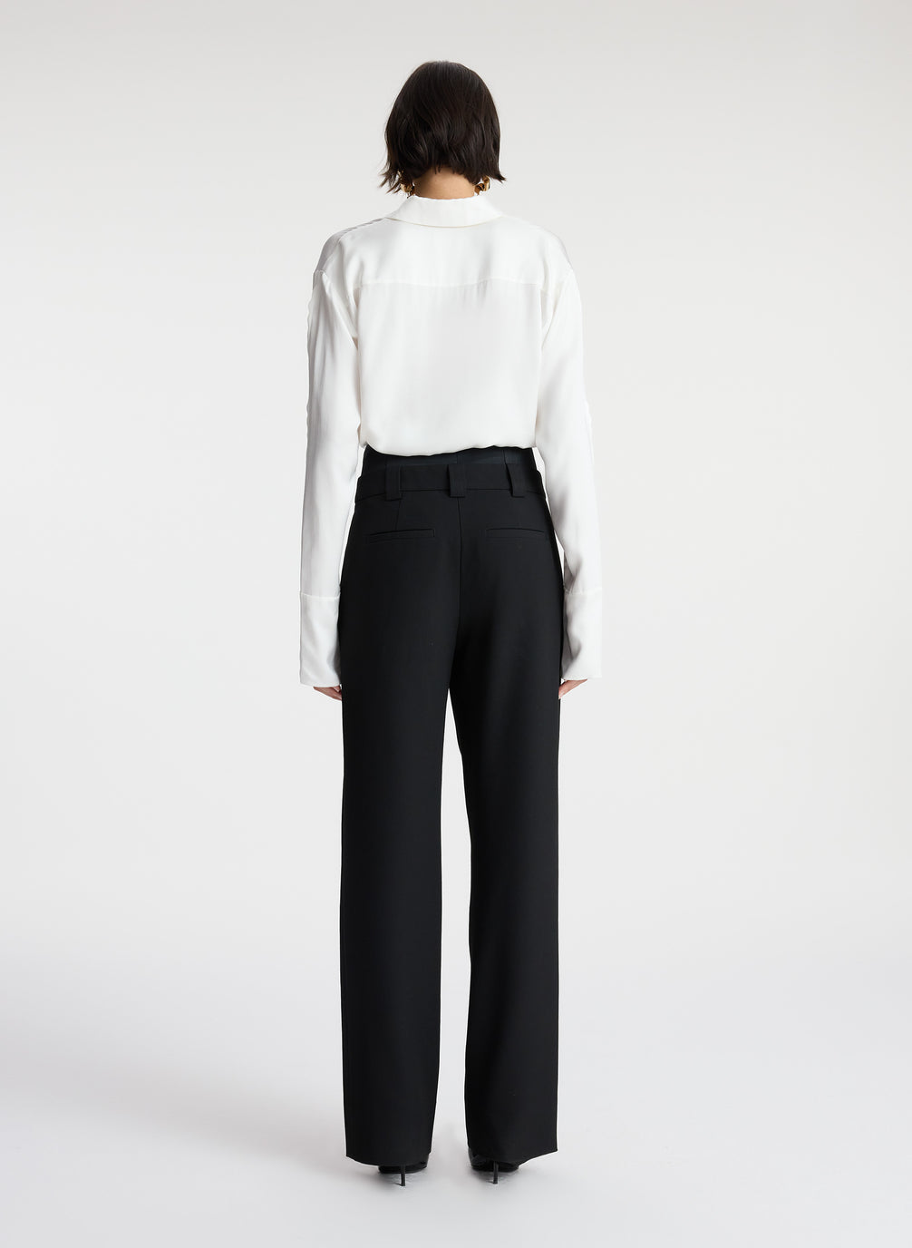 back view of woman wearing white scalloped detailed long sleeve top and black pants