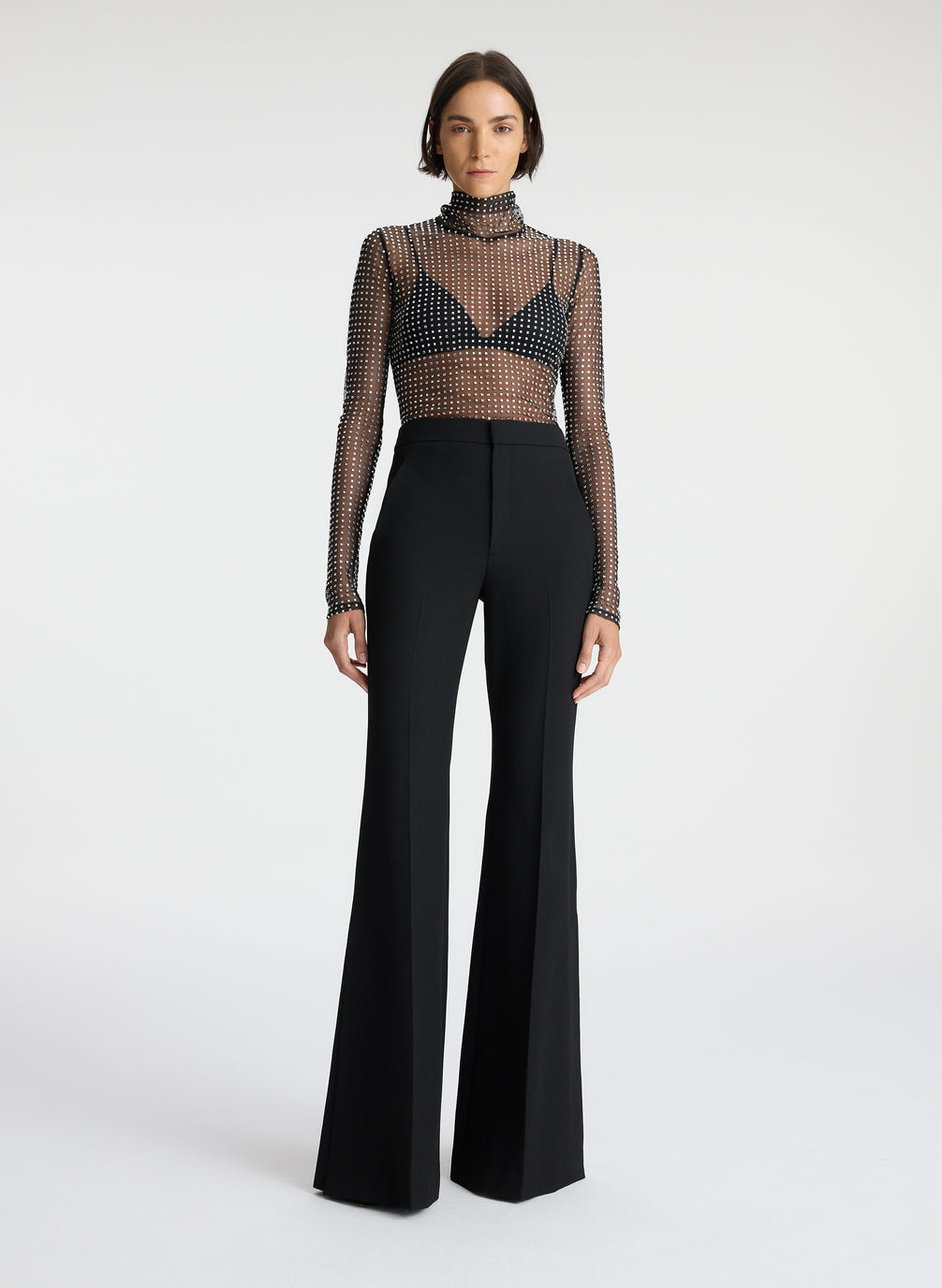 front view of woman wearing sheer black mock neck long sleeve with allover rhinestone embellishment and black pants