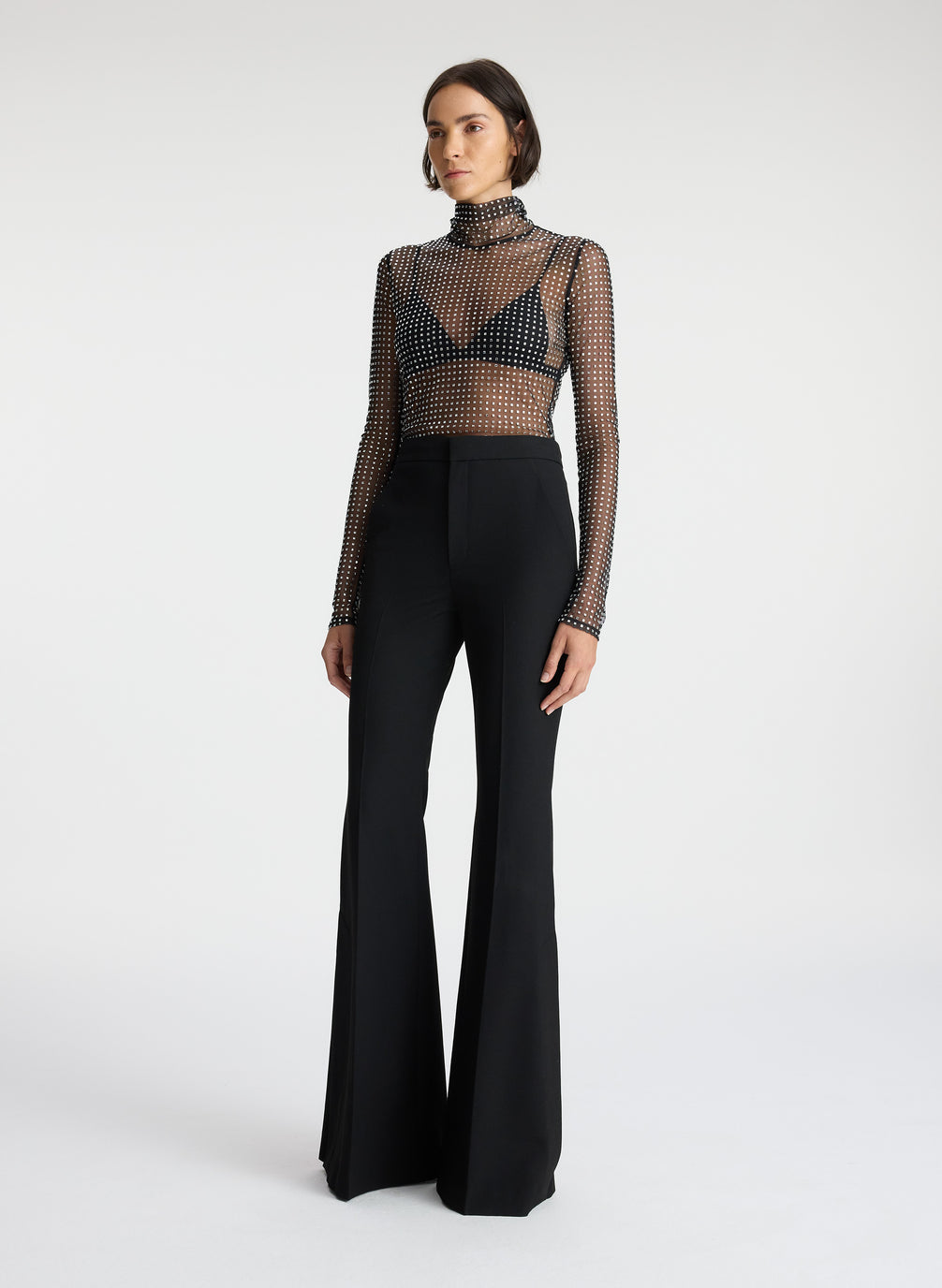 side view of woman wearing sheer black mock neck long sleeve with allover rhinestone embellishment and black pants