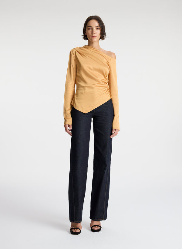 front view of woman wearing asymmetric gold satin long sleeve top and dark wash denim jeans