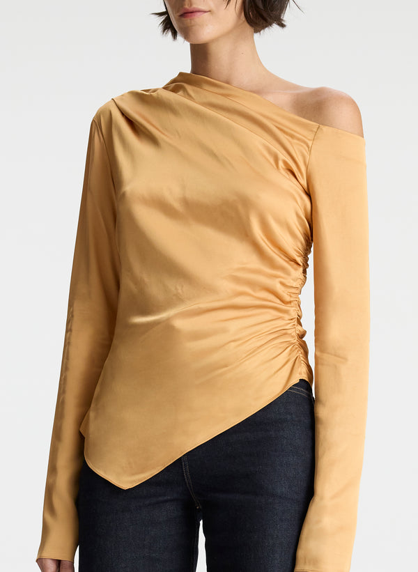 detail view of woman wearing asymmetric gold satin long sleeve top and dark wash denim jeans
