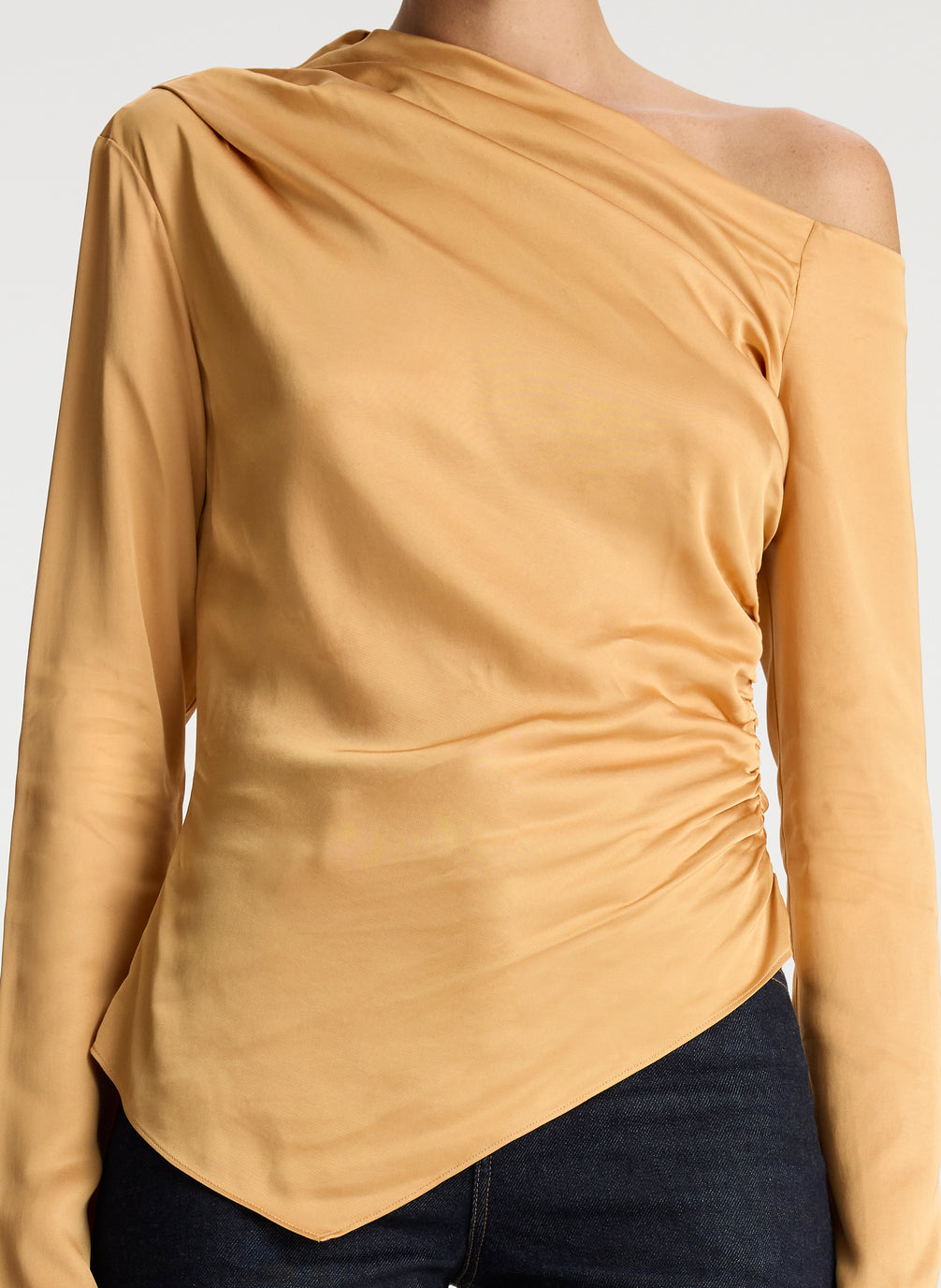 detail view of woman wearing asymmetric gold satin long sleeve top and dark wash denim jeans