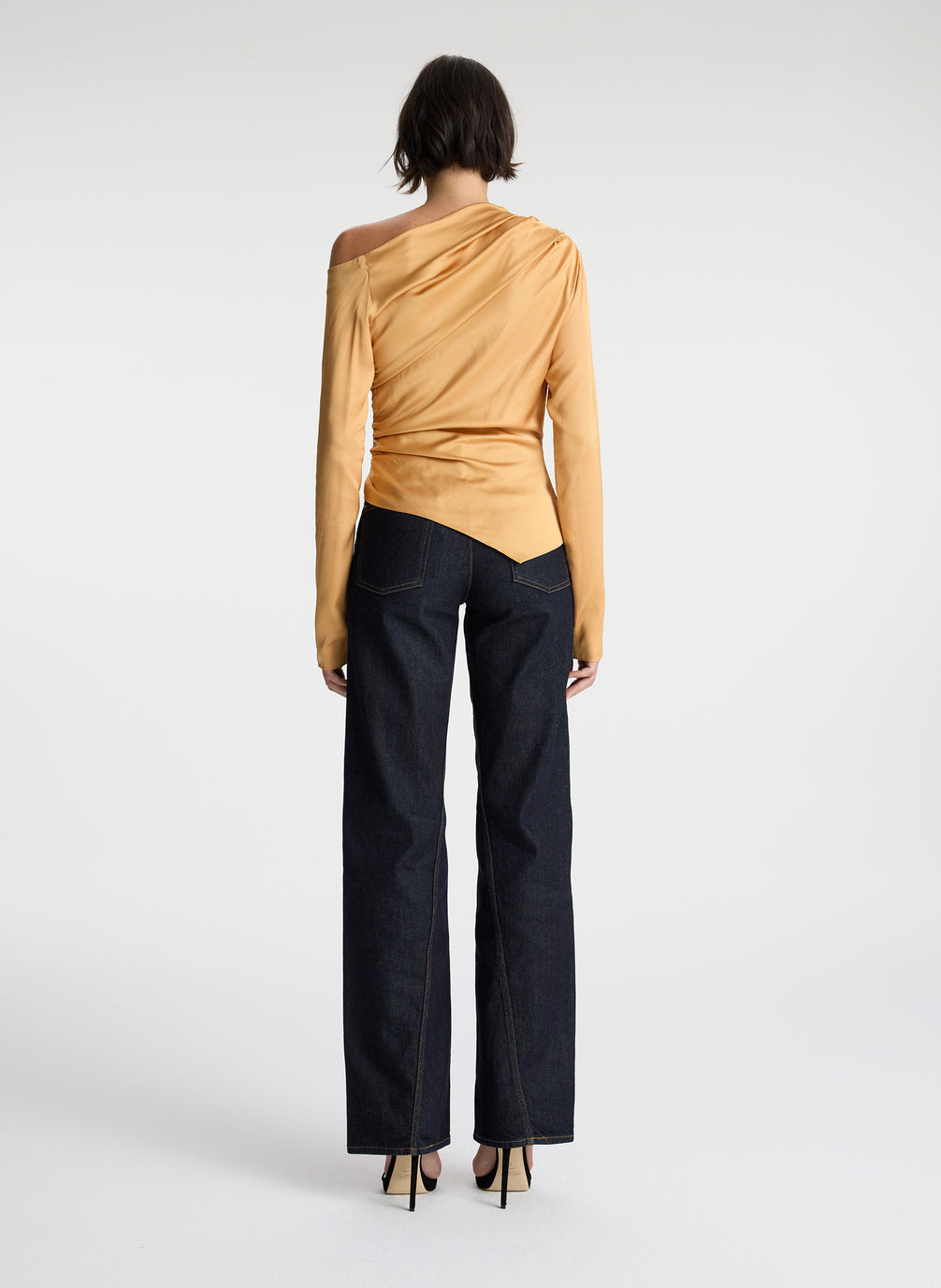 back view of woman wearing asymmetric gold satin long sleeve top and dark wash denim jeans