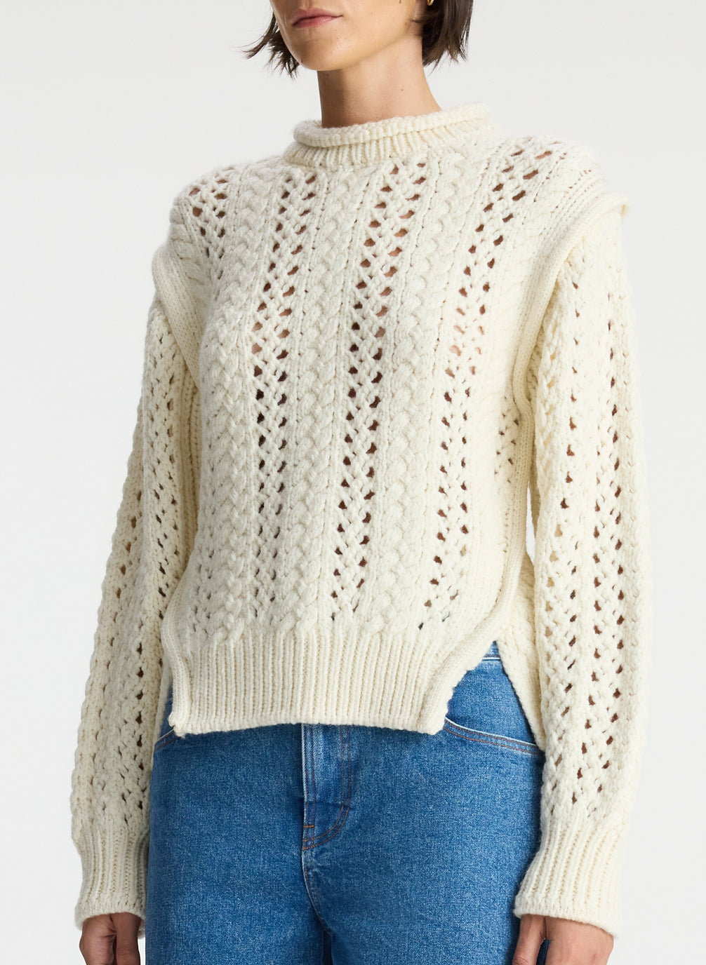 detail view of woman wearing cream open knit sweater and medium wash denim jeans