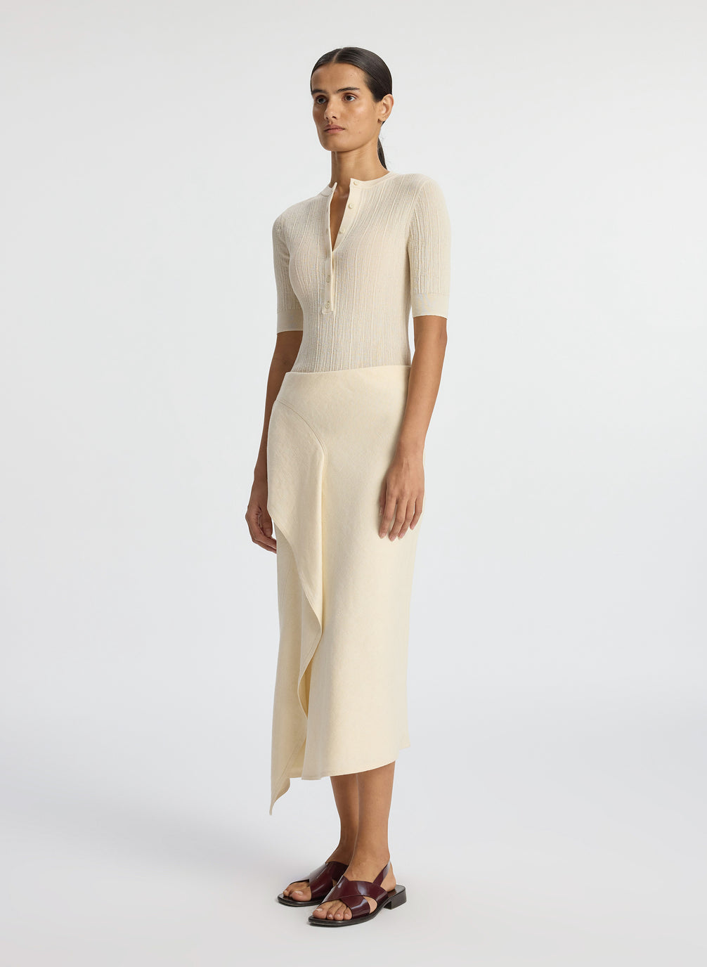 side view of woman wearing beige short sleeve shirt and cream midi skirt