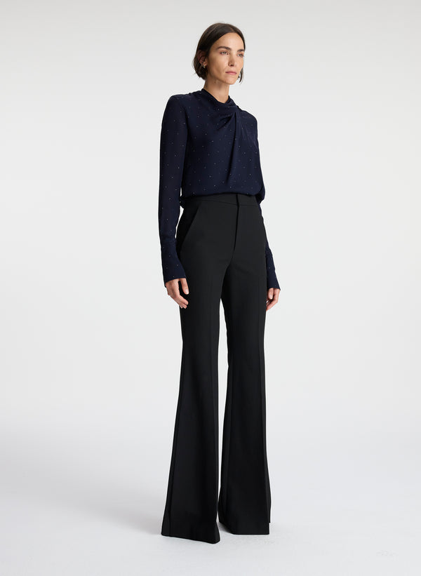 side view of woman wearing navy blue silk long sleeve top with crystal embellishments and black pants