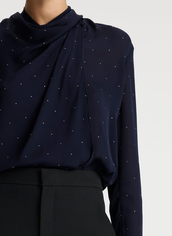 detail view of woman wearing navy blue silk long sleeve top with crystal embellishments and black pants