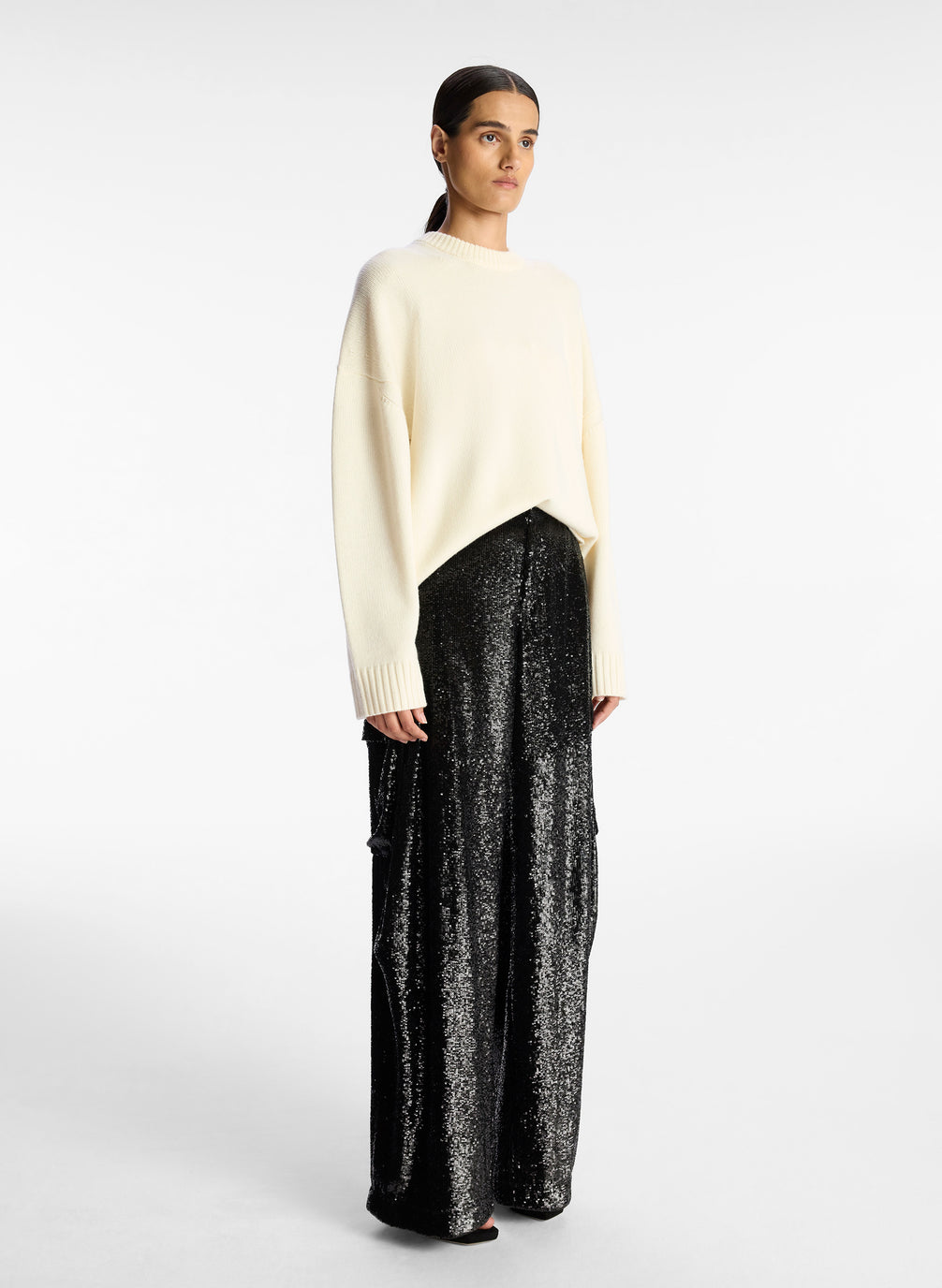 side view of woman wearing cream sweater and black sequined cargo pants