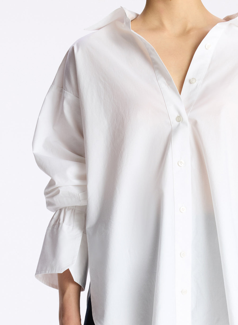 detail view of woman wearing white oversized button down shirt and dark wash denim jeans