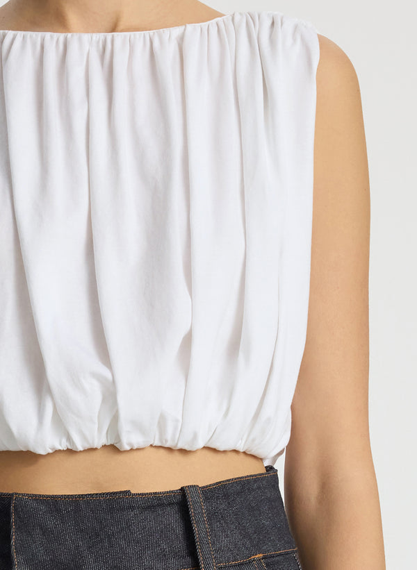 detail view of woman wearing white cropped sleeveless top and raw denim jeans