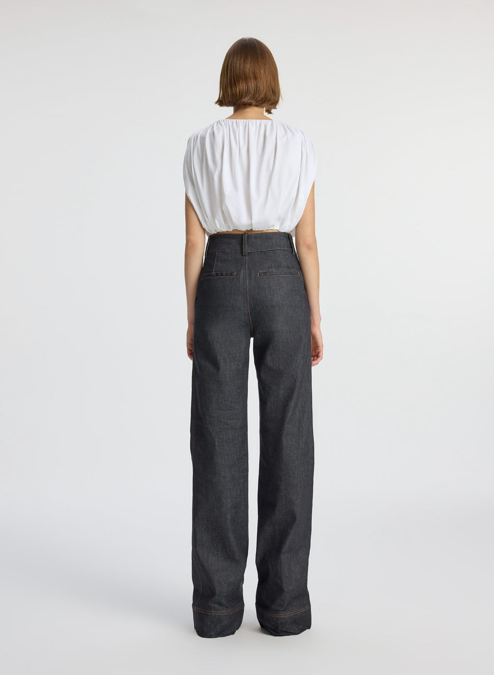 back view of woman wearing white cropped sleeveless top and raw denim jeans
