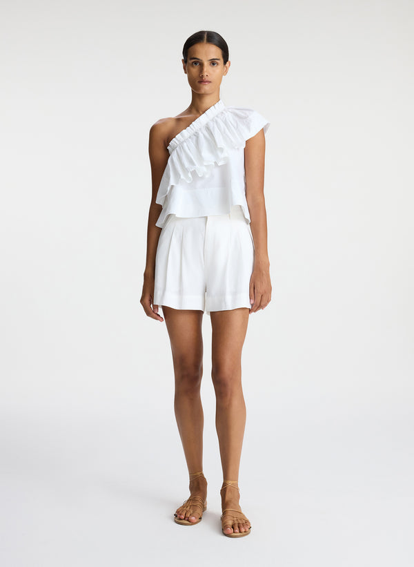 front view of woman wearing white one shoulder ruffle top and white shorts