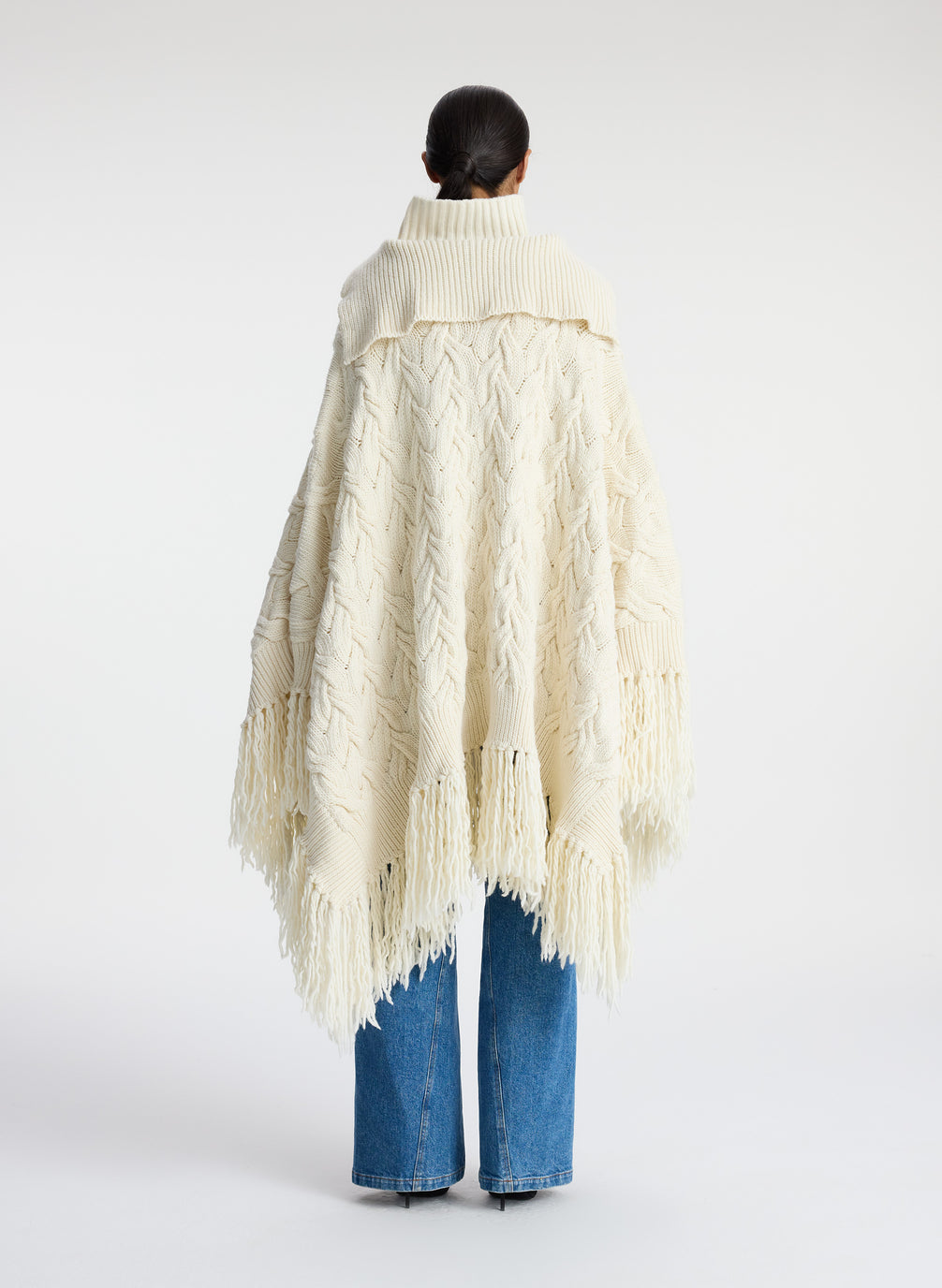 back view of woman wearing cream cable knit poncho with fringe