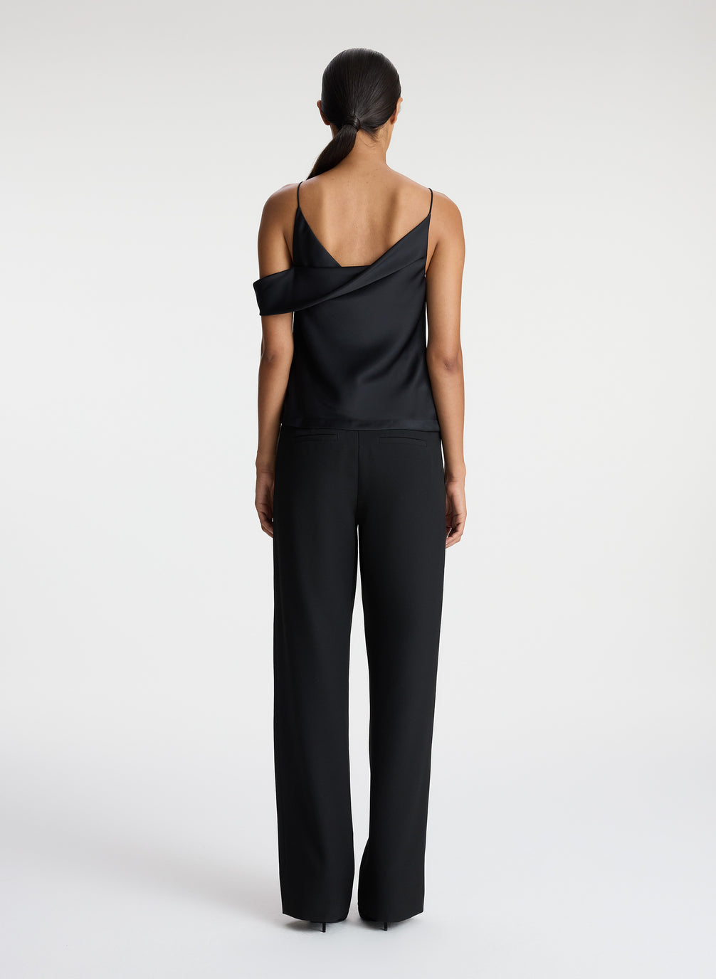 back view of woman wearing black satin asymmetric top with black pants