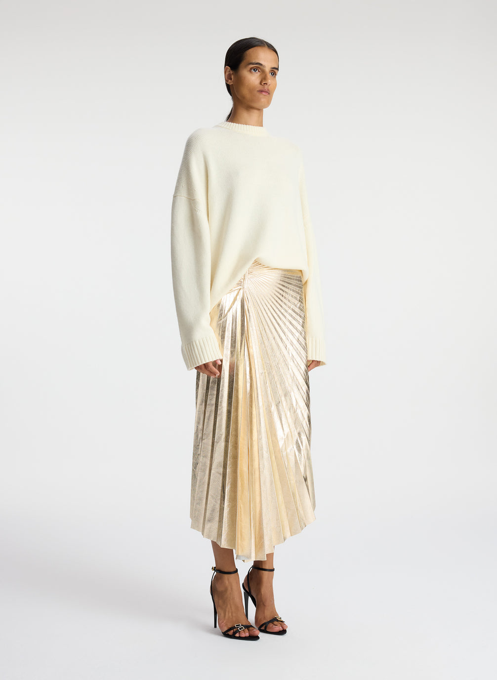 side view of woman wearing white sweated and metallic gold pleated midi skirt