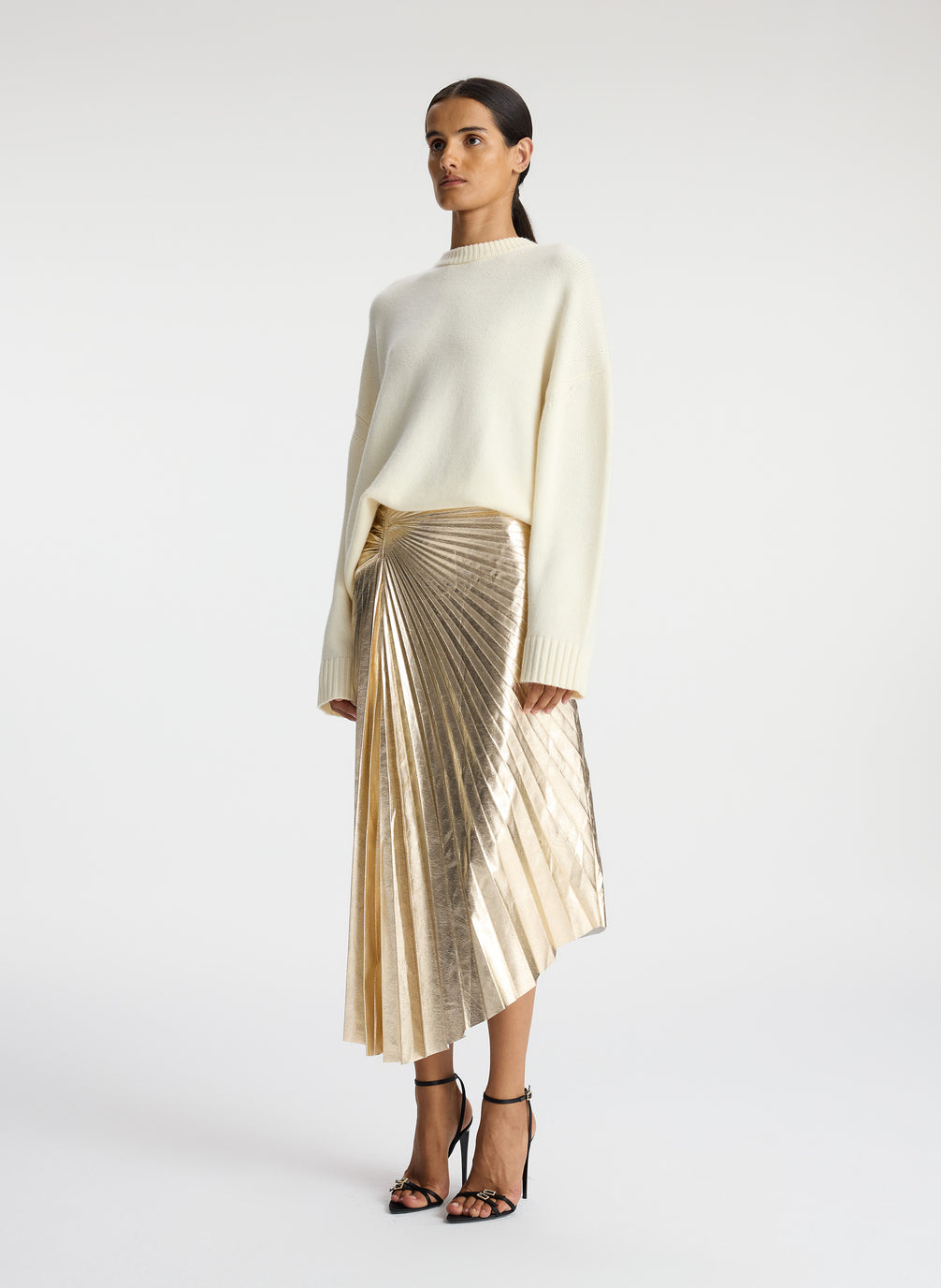 side view of woman wearing white sweated and metallic gold pleated midi skirt
