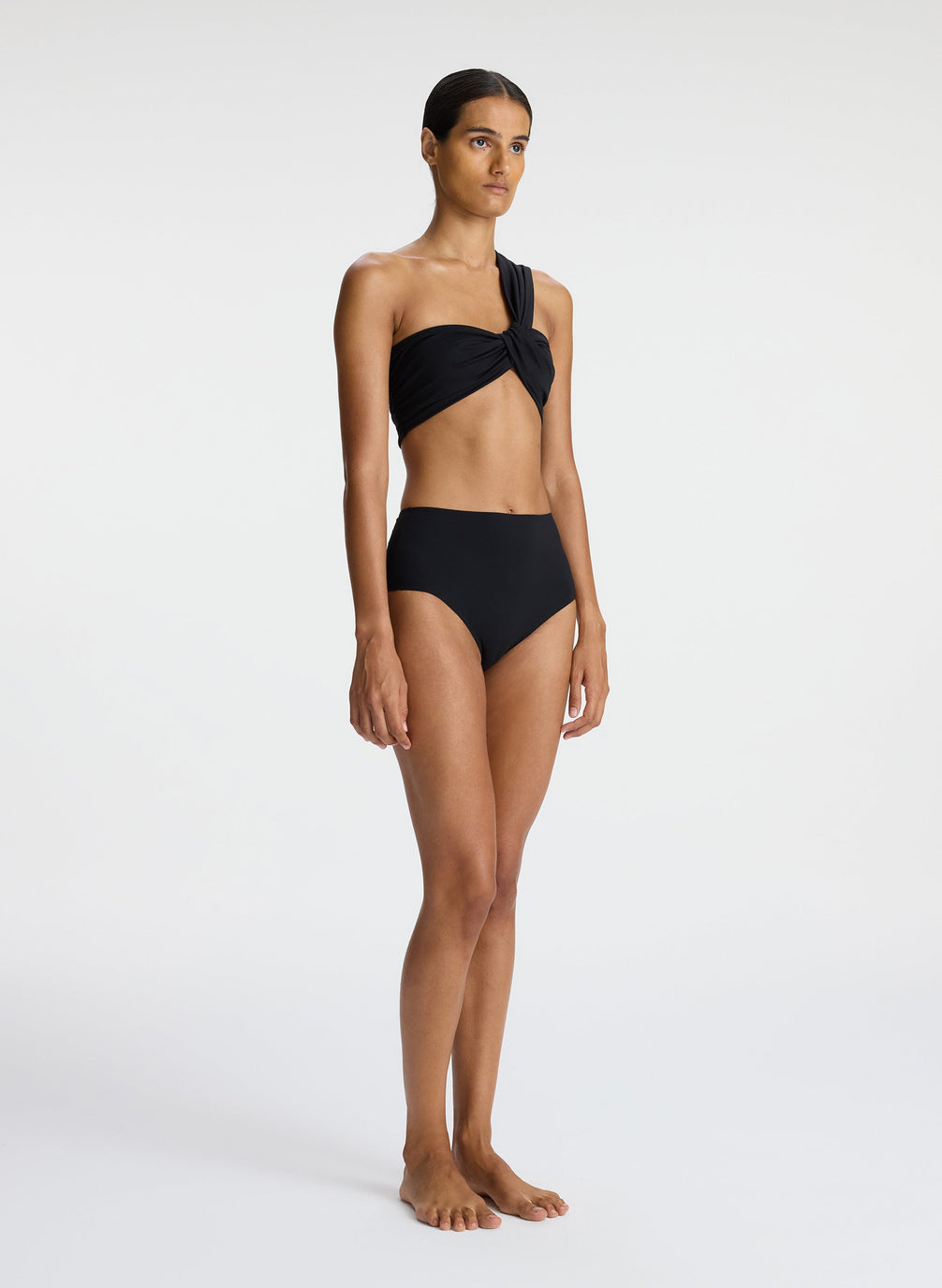 side view of woman wearing black one shoulder swim top and black bikini bottom'