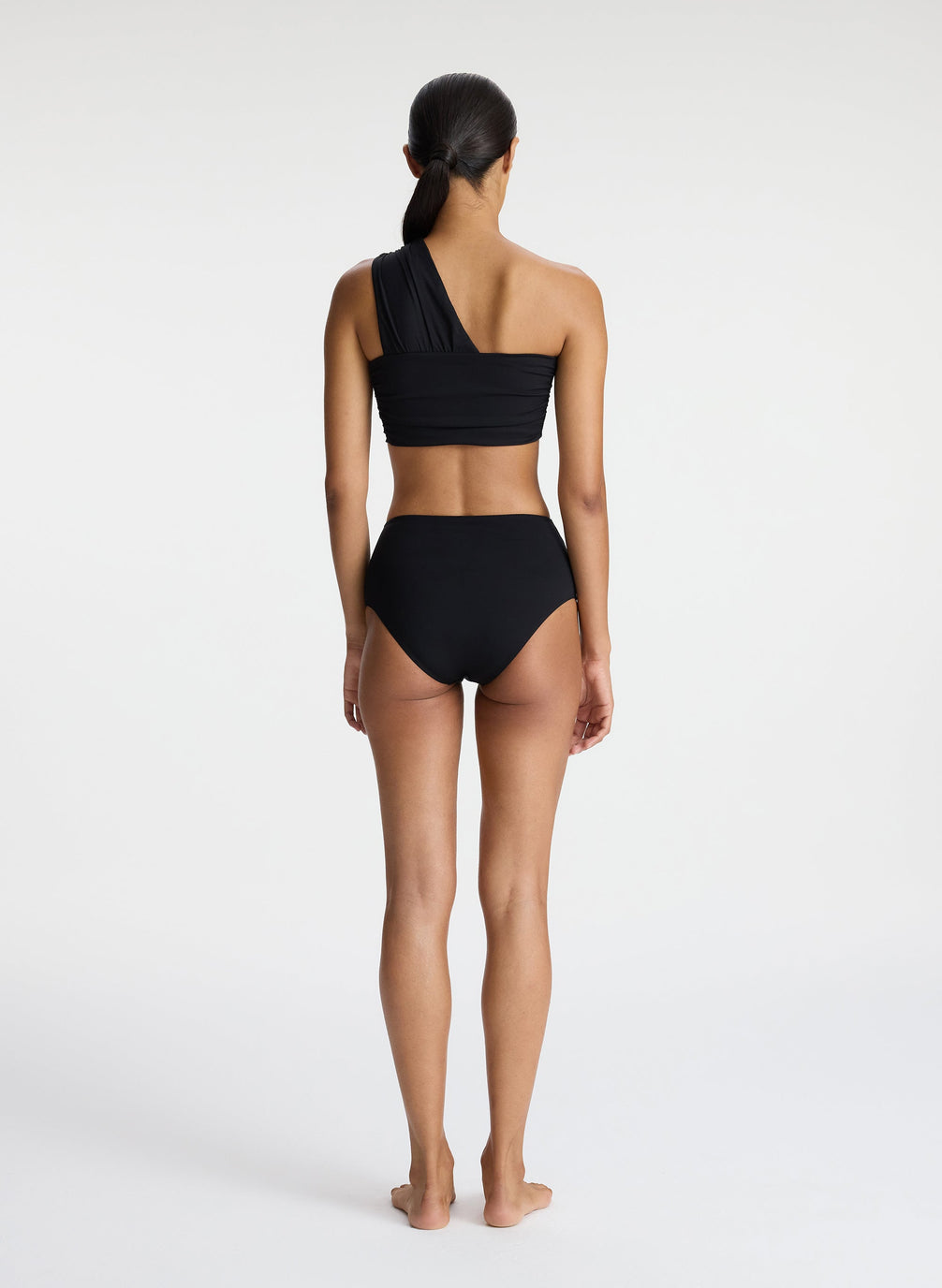back view of woman wearing black one shoulder swim top and black bikini bottom