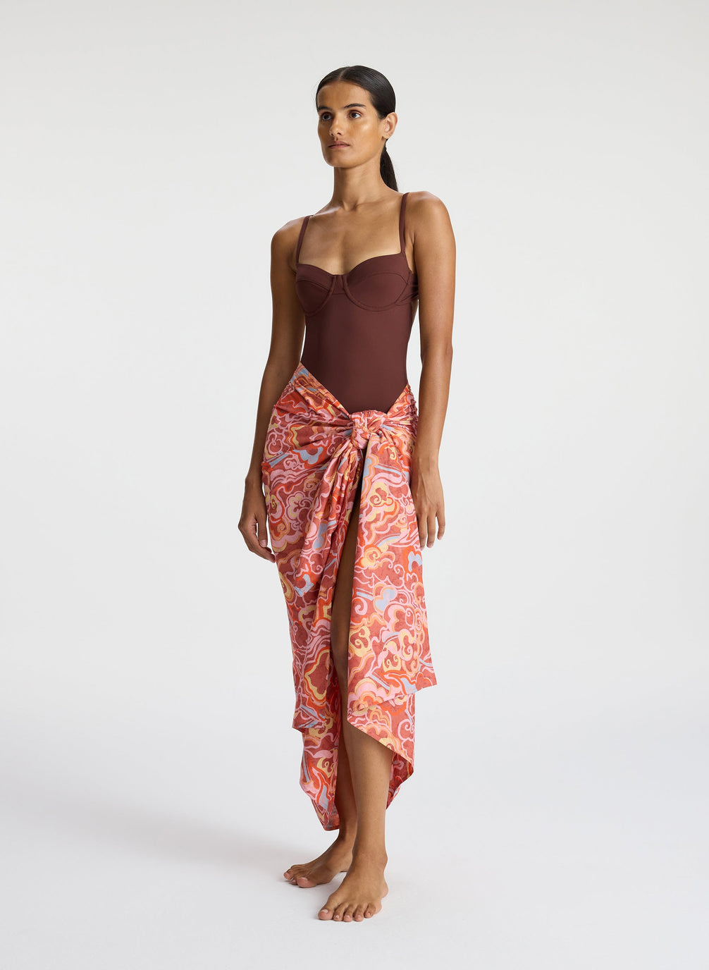 side view of woman wearing brown one piece swimsuit and multicolor sarong