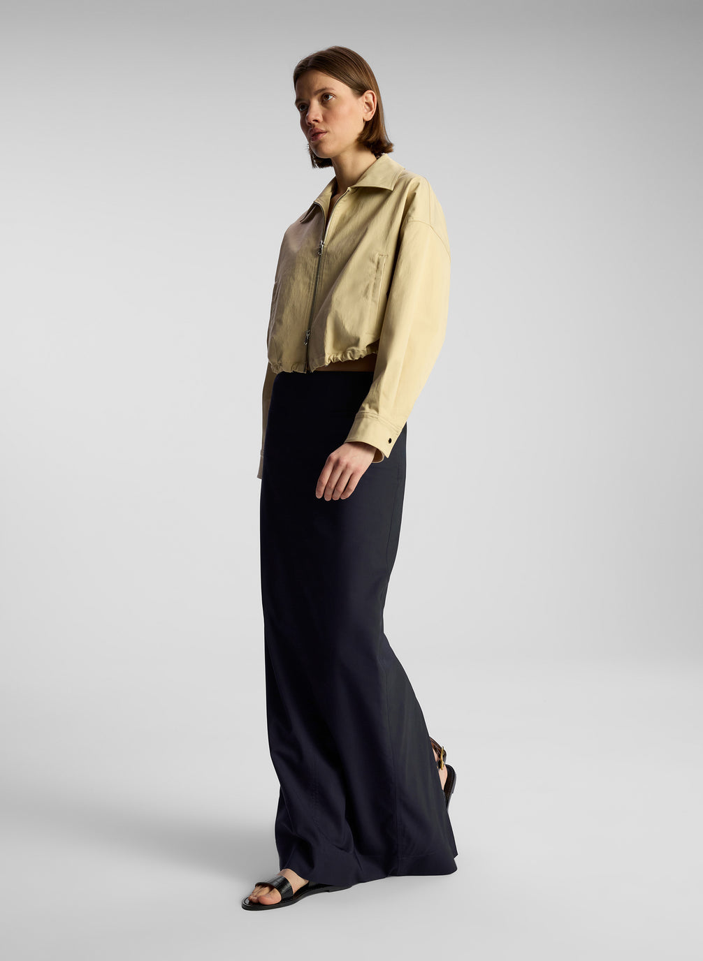 side view of woman wearing tan jacket and navy blue maxi skirt