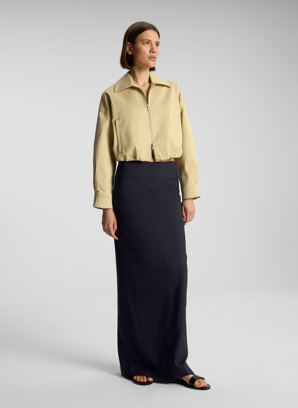 side view of woman wearing tan jacket and navy blue maxi skirt