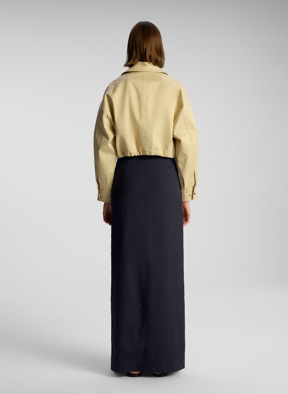 back view of woman wearing tan jacket and navy blue maxi skirt