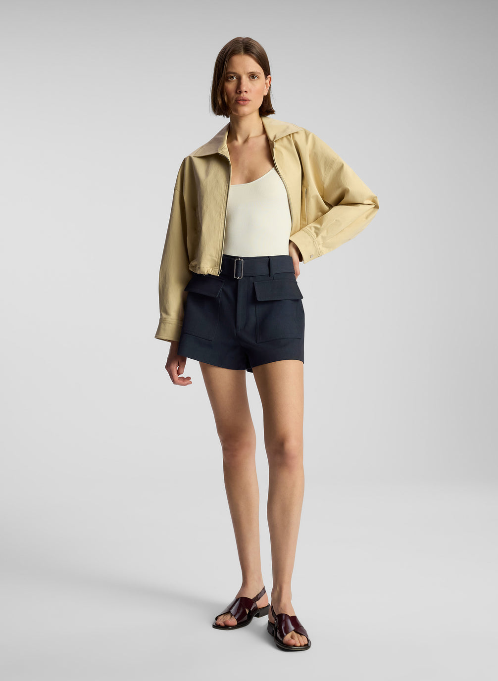 front view of woman wearing tan jacket, cream bodysuit, and navy blue shorts