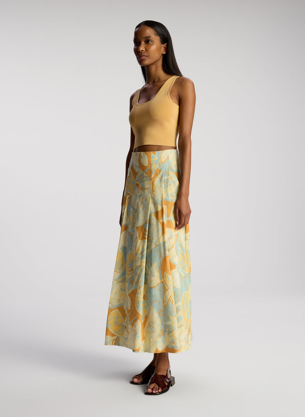 side view of woman wearing tan sleeveless top with multicolor printed midi skirt