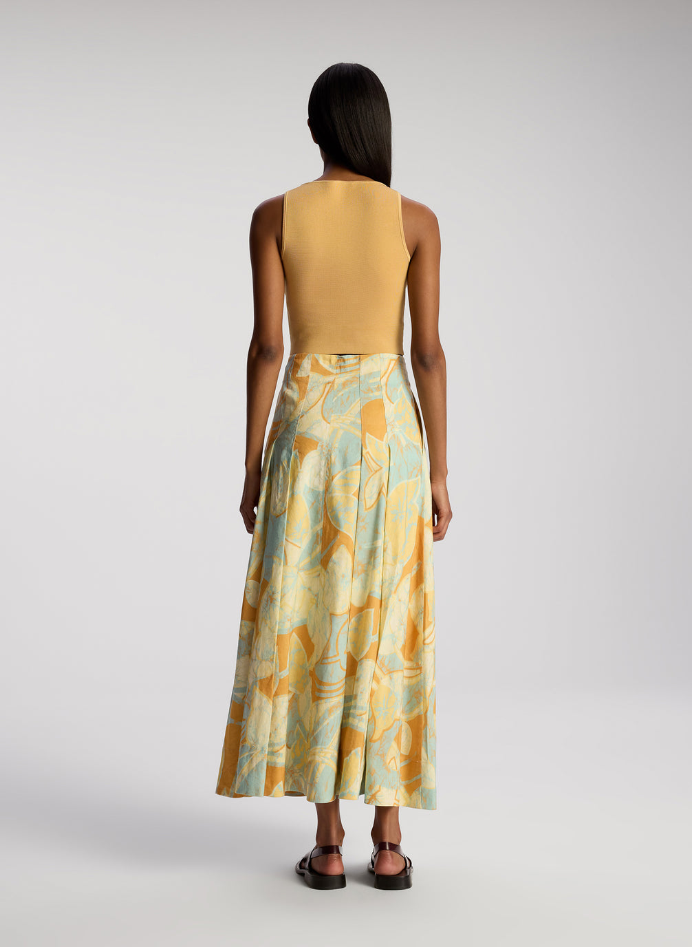 back view of woman wearing tan sleeveless top with multicolor printed midi skirt