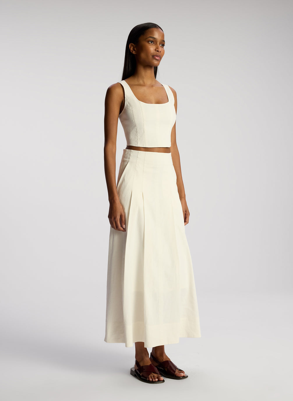 side view of woman wearing white sleeveless cropped top and white midi skirt