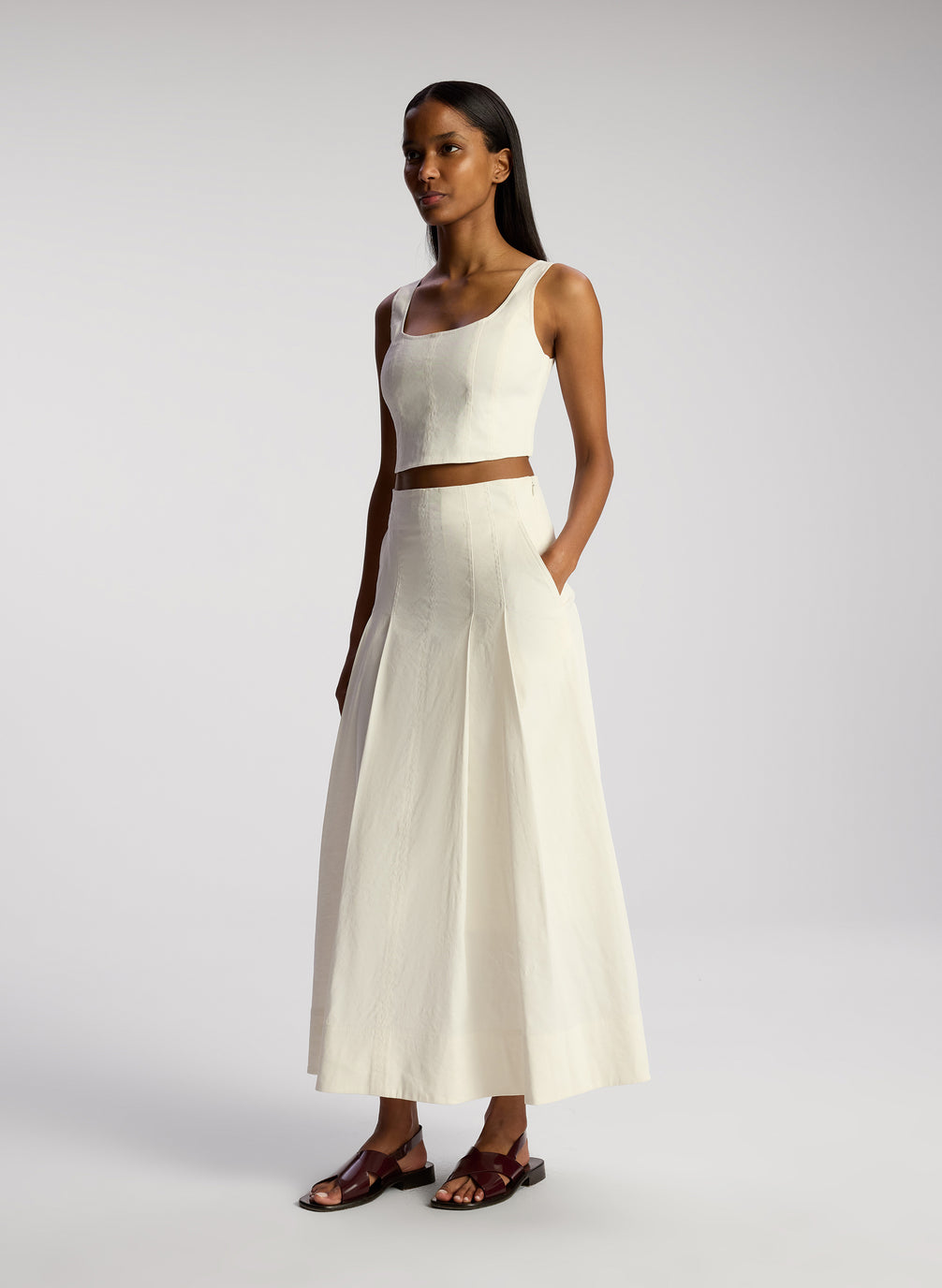side view of woman wearing white sleeveless cropped top and white midi skirt