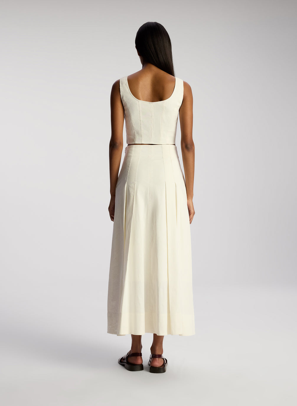 back view of woman wearing white sleeveless cropped top and white midi skirt