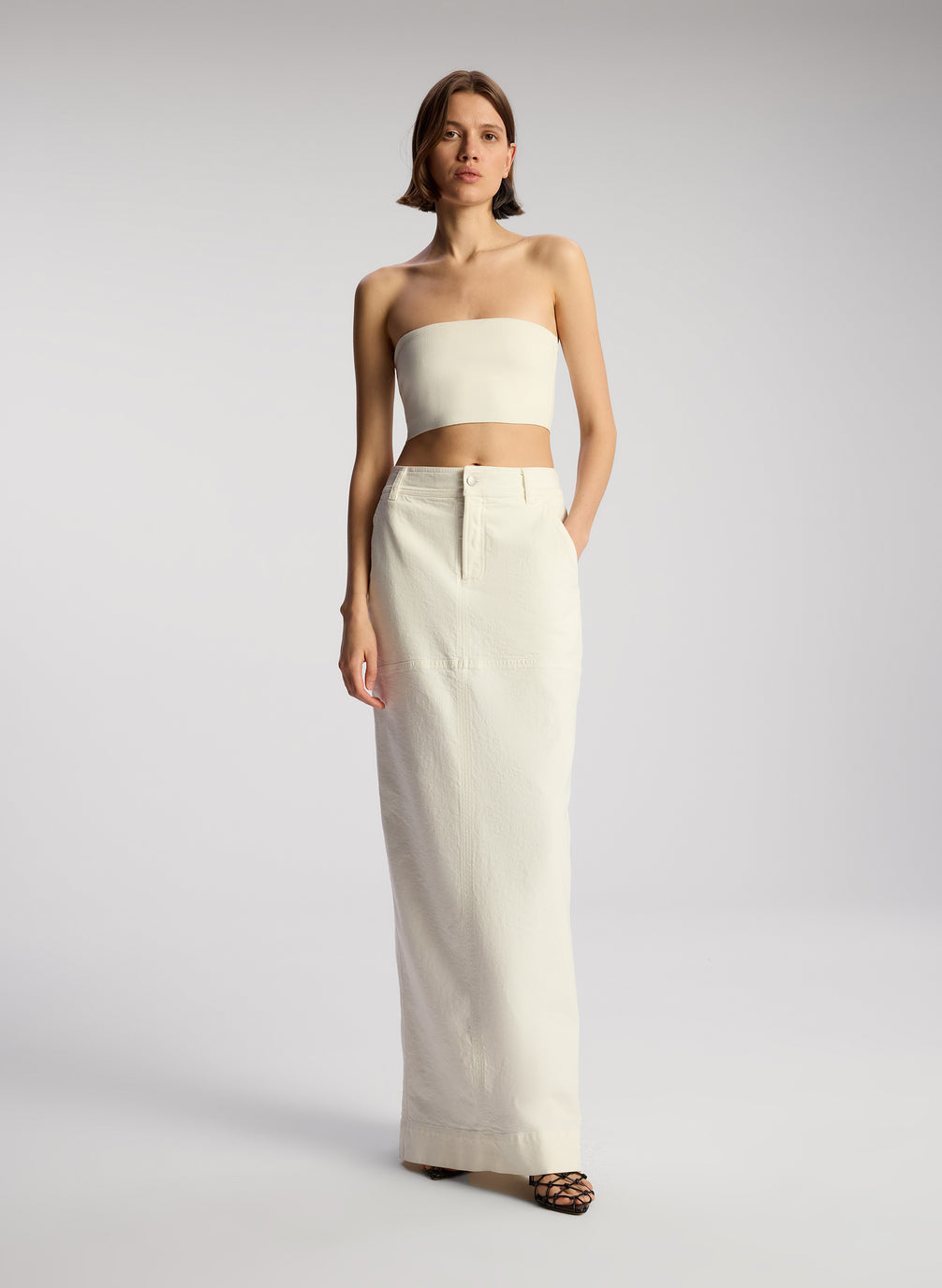 front view of woman wearing off white cropped strapless top with white maxi skirt