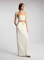 side view of woman wearing off white cropped strapless top with white maxi skirt